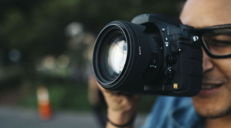 Man looking through camera lens wearing glasses